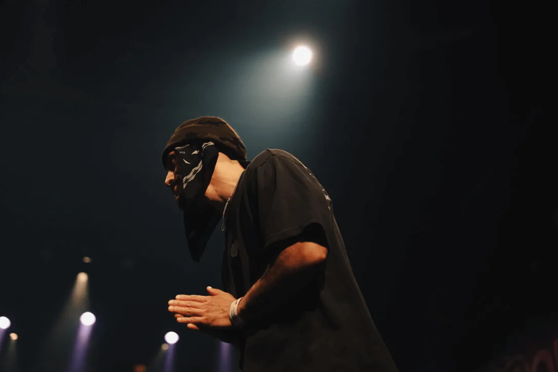 A masked figure bowing under stage light.